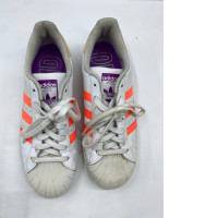  white Adidas Superstar sneakers with bright orange three-stripes and purple accents. 