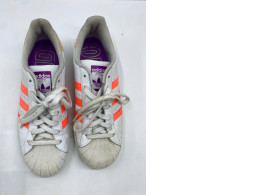 white Adidas Superstar sneakers with bright orange three-stripes and purple accents. white Adidas Superstar sneakers with bright orange three-stripes and purple accents.