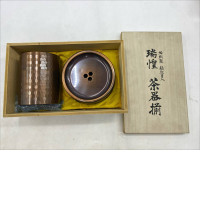 A copper tea set, especially a Suiho (瑞惶) style tea set, a traditional Japanese tea set, would likely consist of a tea box (a tall container with a lid) and a tea saucer (a wider, shallower bowl) inside a wooden box.