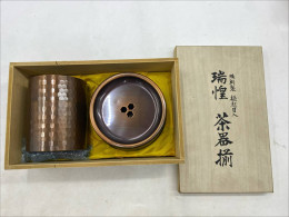 A copper tea set, especially a Suiho (瑞惶) style tea set, a traditional Japanese tea set, would likely consist of a tea box (a tall container with a lid) and a tea saucer (a wider, shallower bowl) inside a wooden box.