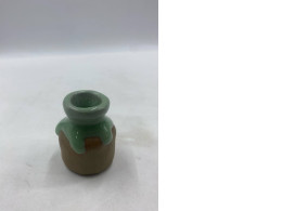 A small sculpture, glazed green on the neck and shoulders, resembles a miniature vase or pot.