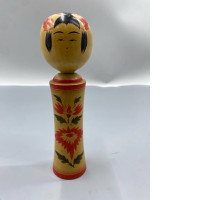 vintage Japanese Kokeshi doll is a traditional wooden figurine, likely from the Naruko region, featuring hand-painted red floral motifs and a distinct round head. 
