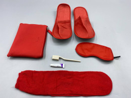 A red hotel amenity set, consisting of a storage bag, slippers, eye mask, toothbrush, and toothpaste.
